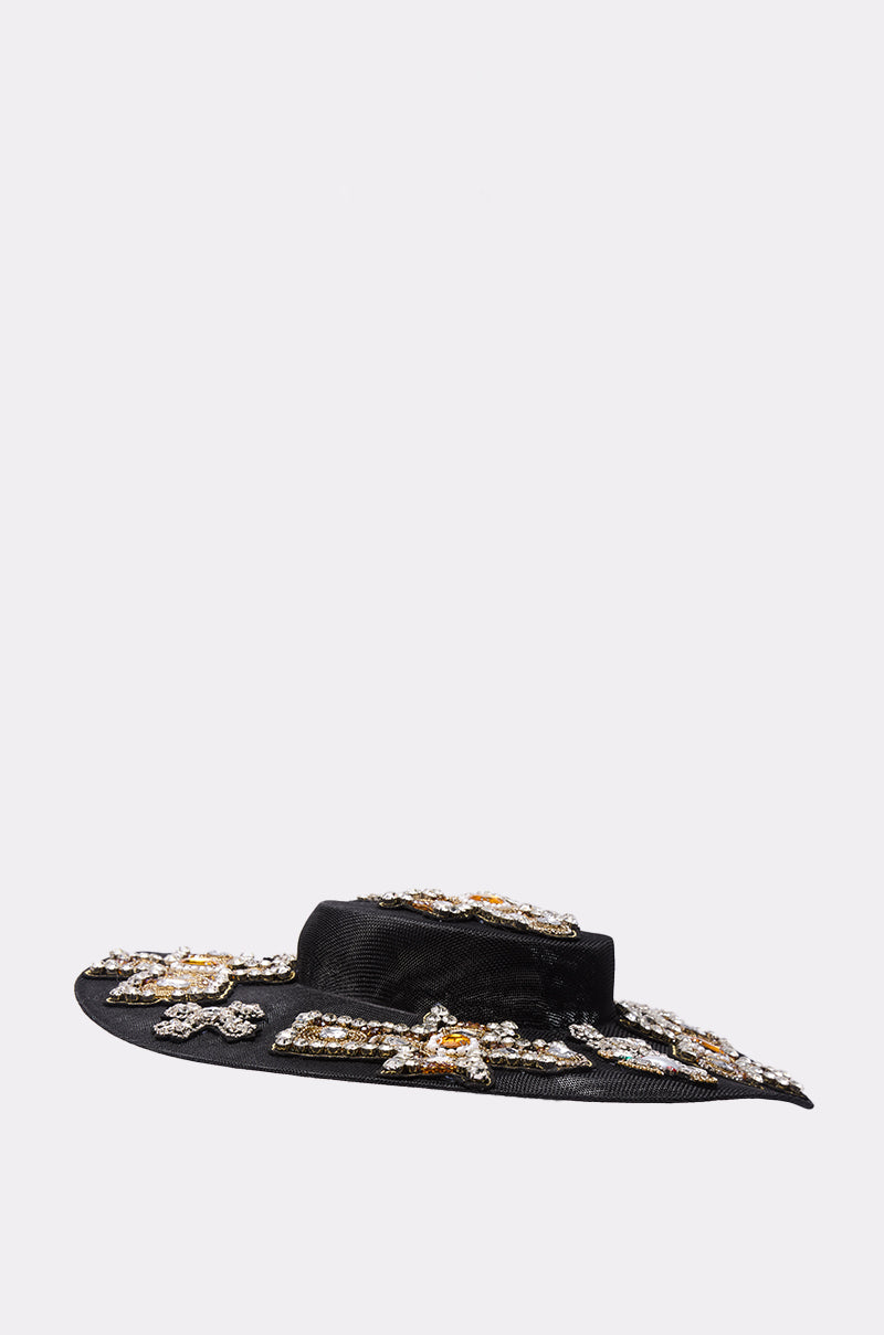 The STAY BLESSED CLIP ON HAT is a wide-brimmed black hat featuring sparkling crystal and gemstone embellishments, making a bold statement against a plain light gray background.