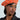 Wearing the COME ALIVE GROMMET BERET, a person pairs it flawlessly with a pinstripe blazer. Their bold blush makeup enhances the chic outfit as they look slightly to the side against a simple, light-colored backdrop.