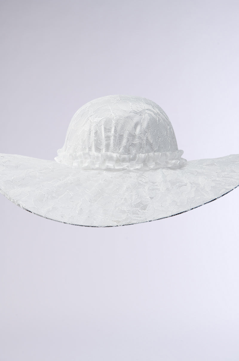 The I AM IT LACE HAT is a large, elegant white hat with a woven texture, featuring a wide curved brim and subtle floral lace design. It has a ruched band around the crown, set on a simple gradient background.