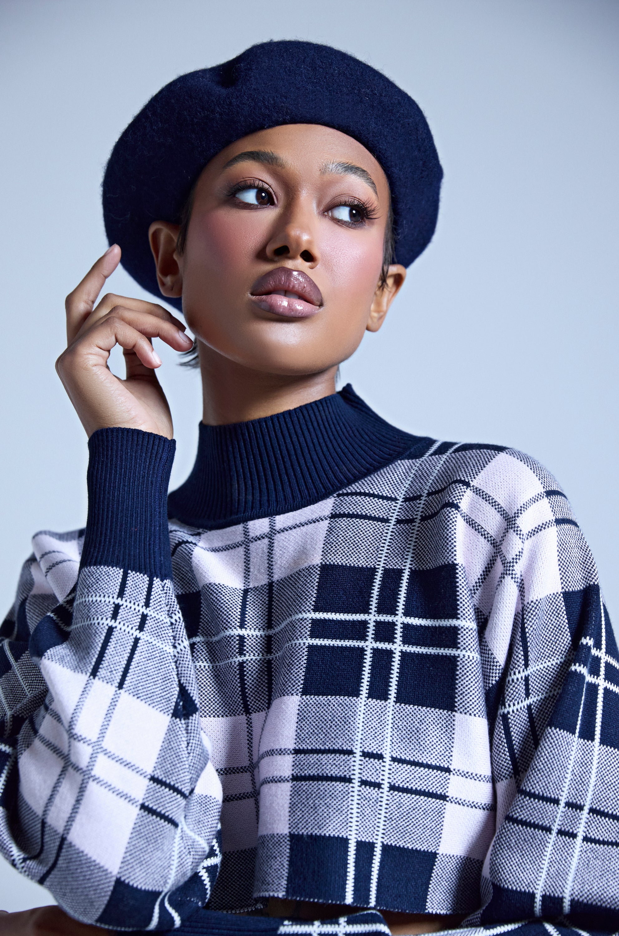 Wearing the TOO COZY NAVY BERET and a plaid turtleneck, a person gazes thoughtfully to the side against a light background. 0