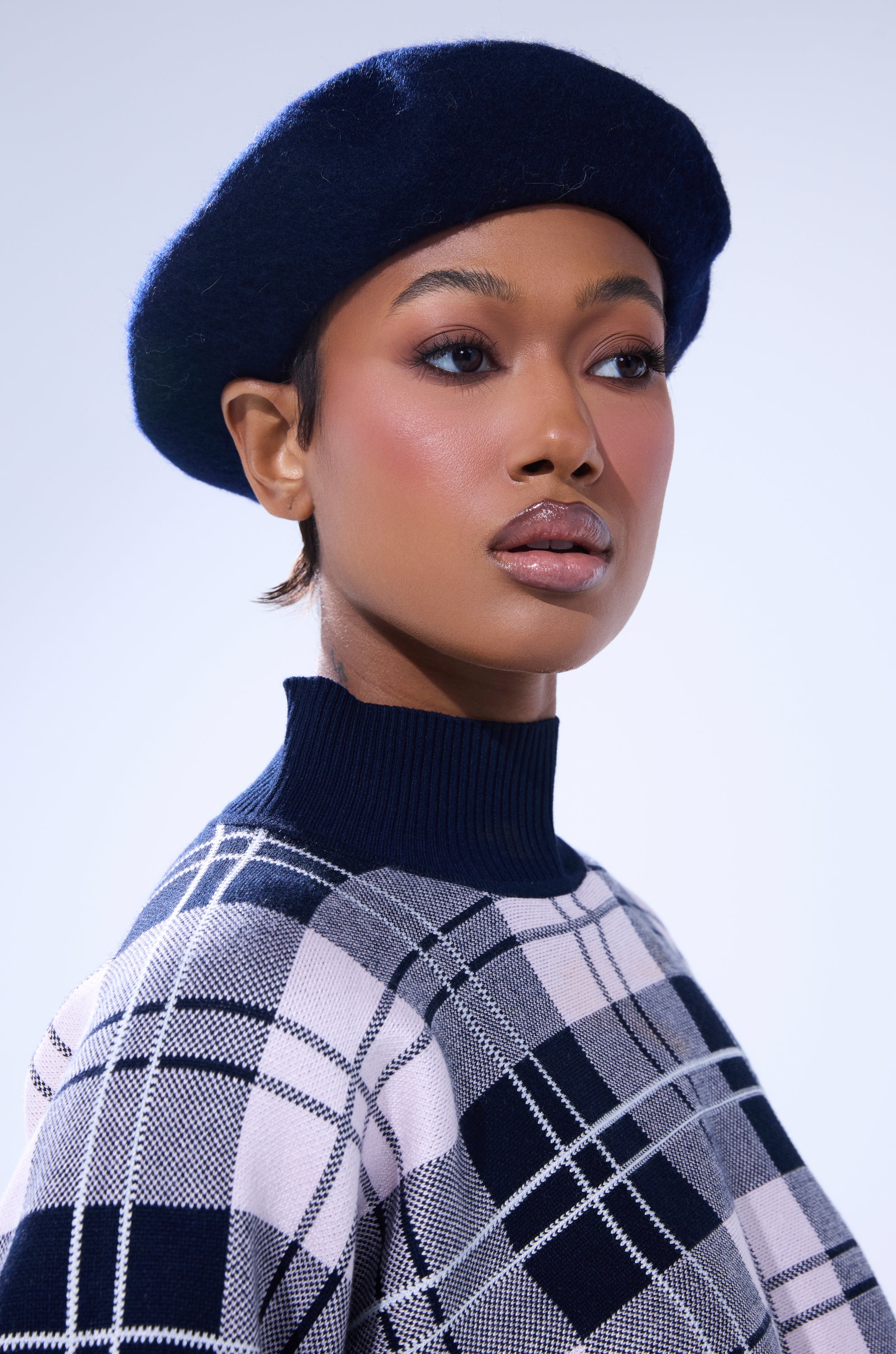 A woman confidently gazes to the side against a light background, wearing the TOO COZY NAVY BERET and a high-collared plaid sweater. Her smooth, glowing skin and glossy lips complete her polished look. 6