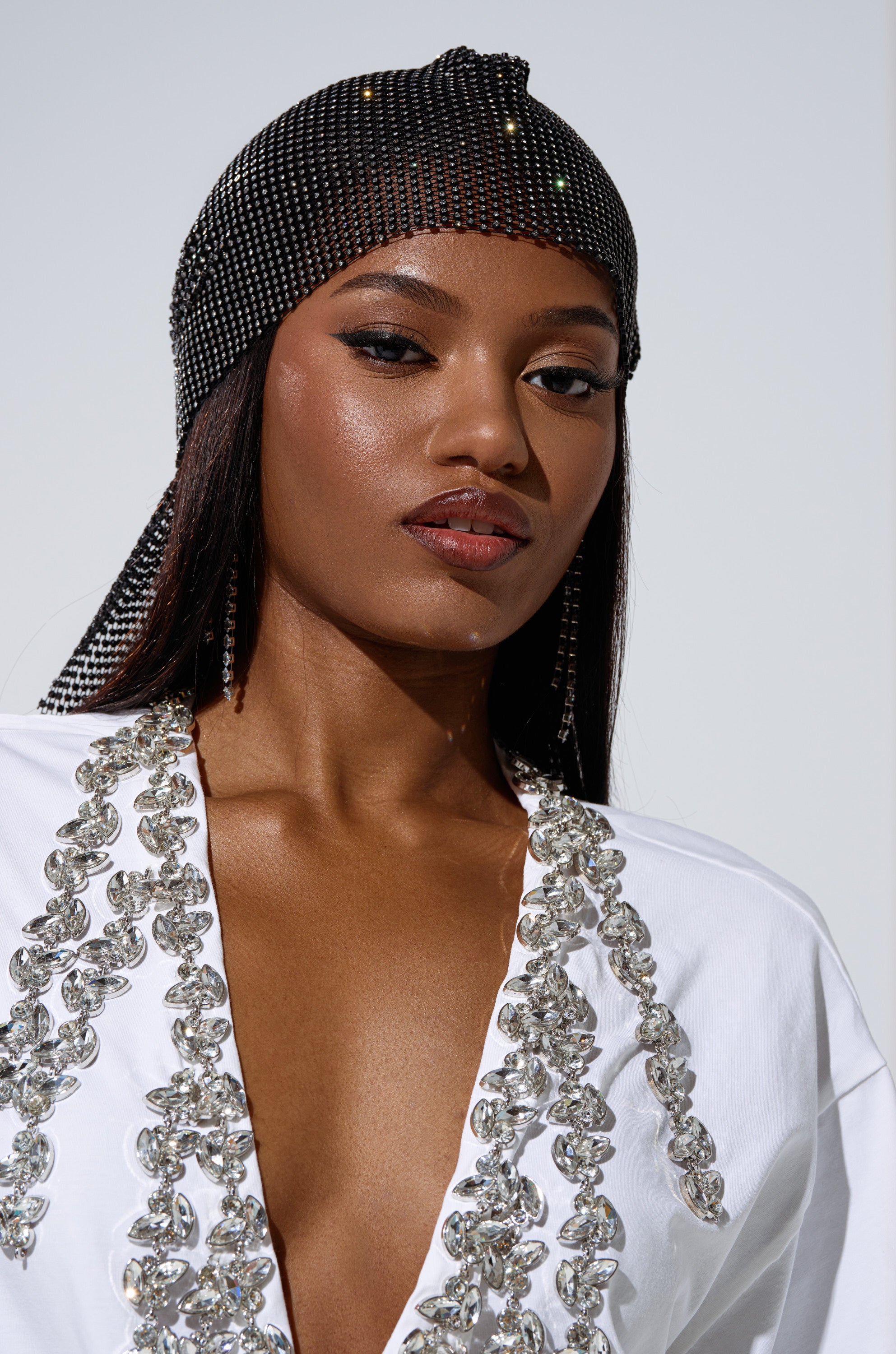 A woman poses confidently against a plain background wearing the ONLY THE ELITE RHINESTONE NET DURAG and a white garment with intricate silver details.