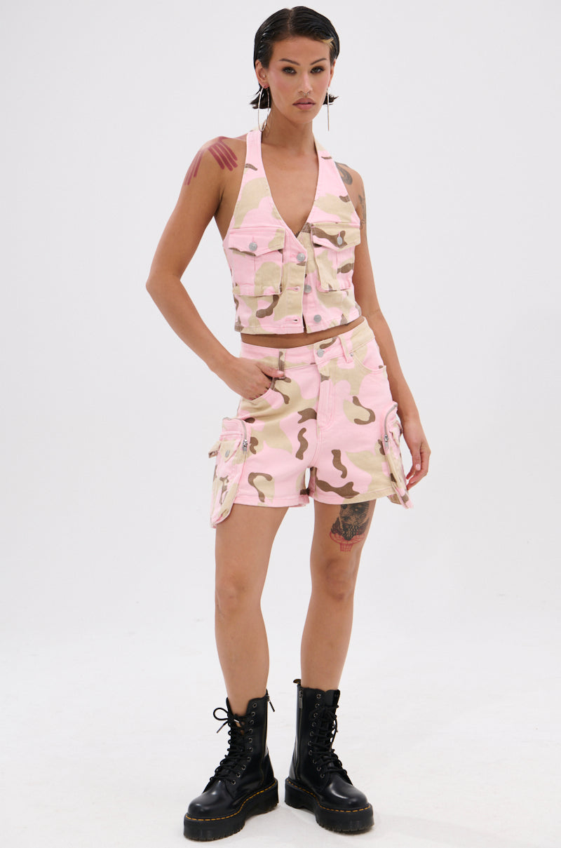 A person with short dark hair models the GIRL POWER CAMO CARGO SHORT in pink and beige with a matching vest and black lace-up boots, standing confidently against a plain white background.