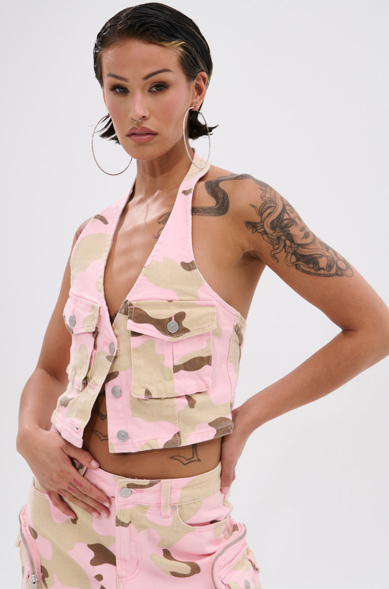 A woman with slicked-back hair and hoop earrings models the GIRL POWER CAMO BUTTON DOWN HALTER TOP with matching pants. She shows off tattoos on her arm and poses confidently against a plain background. 0