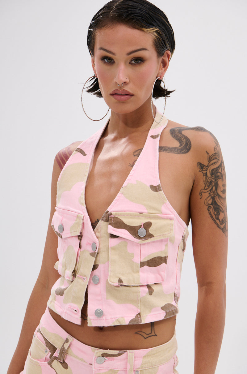A woman with short, slicked-back hair and large hoop earrings models the GIRL POWER CAMO BUTTON DOWN HALTER TOP with matching pants. She shows off several tattoos while posing against a simple, light background. 1