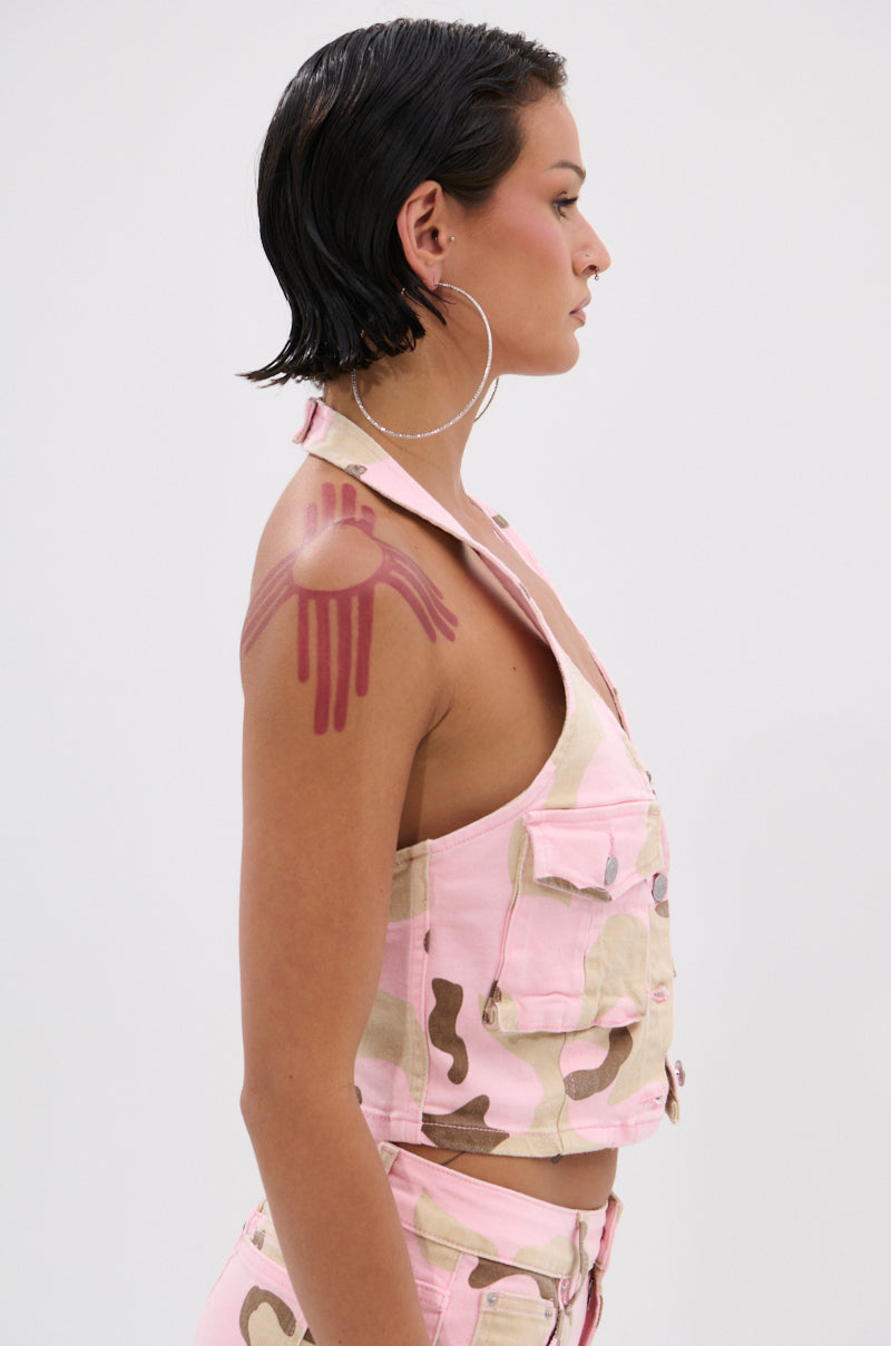 A person with short, wet, dark hair wears large hoop earrings and the GIRL POWER CAMO BUTTON DOWN HALTER TOP and matching pants. A pink jellyfish graphic decorates their upper arm. They stand in profile against a plain background with denim accessories. 2