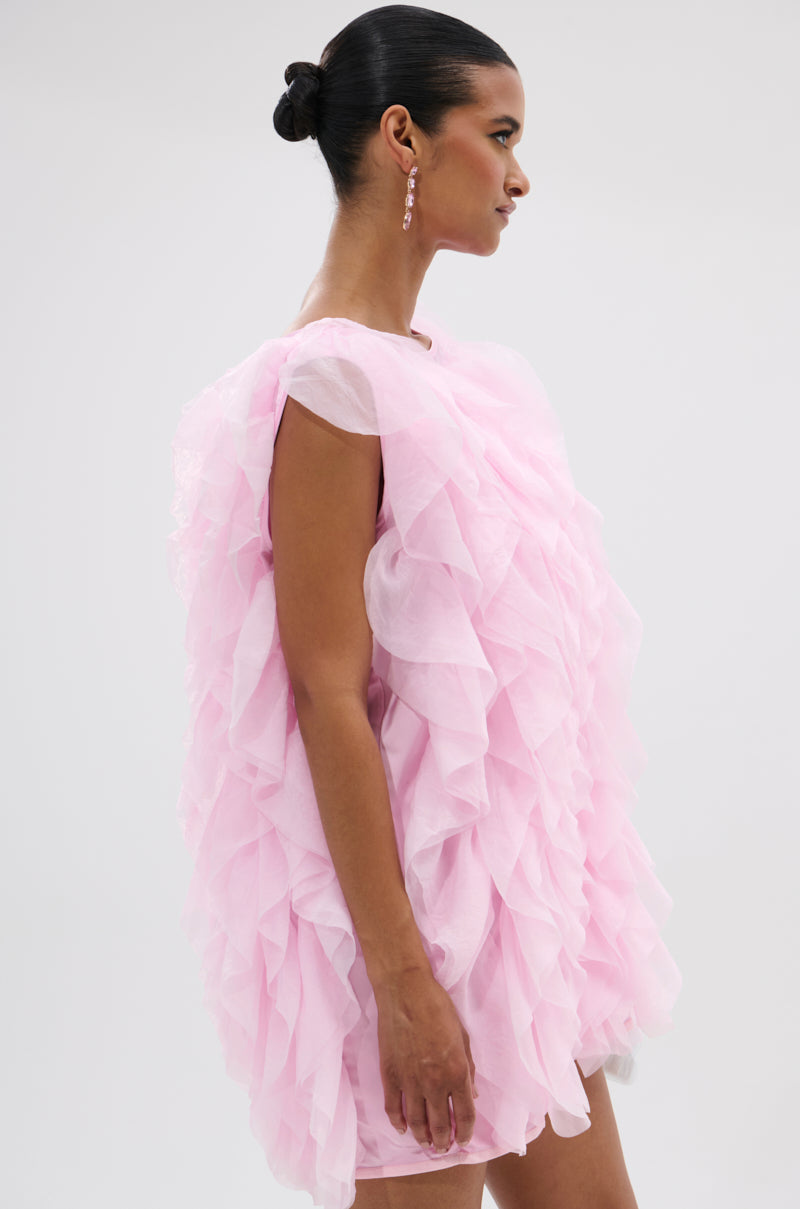 A woman with her hair in a sleek bun wears the LOVER GIRL RUFFLE MINI DRESS, featuring pink organza layered ruffles and dangle earrings, against a plain light background. 3