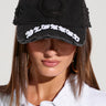 A person is pictured wearing the FEELING BLESSED SNAPBACK, a black cap with distressed detailing and "blessed" embroidered in white letters on the front. The person is also donning a white collared shirt and gold hoop earrings, with their face partially obscured by the cap.