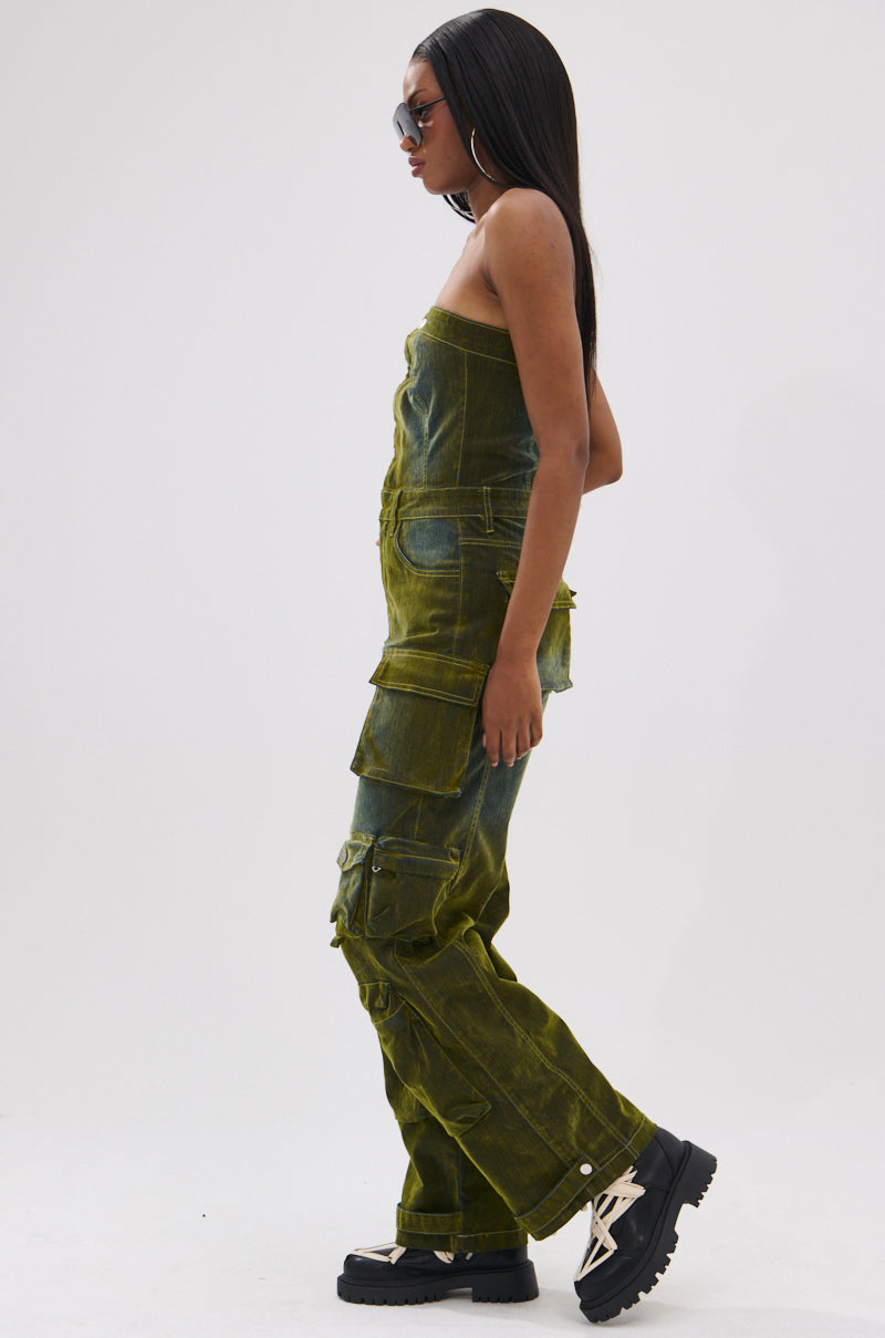 A woman with long straight hair embodies tomboy chic in sunglasses and the MIRA DISTRESSED VELVET DENIM JUMPSUIT. She stands sideways in black chunky platform shoes against a plain white background.