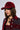 A person with medium-length brown hair is wearing the GIADA DISTRESSED SNAPBACK in red, adorned with silver studs, and a matching red outfit. They have natural makeup and are accessorized with a chunky metal necklace featuring a large pendant. The background is plain white.