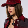 A person with medium-length brown hair is wearing the GIADA DISTRESSED SNAPBACK in red, adorned with silver studs, and a matching red outfit. They have natural makeup and are accessorized with a chunky metal necklace featuring a large pendant. The background is plain white.