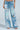 A model wears the PICKING PETALS FLORAL AND LACE DETAIL DENIM PANTS with distressed rips, white lace, a high waist, and a loose fit, styled with open-toe heels against a light blue background.