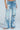 A person wears PICKING PETALS FLORAL AND LACE DETAIL DENIM PANTS—light blue, high-waisted, wide-leg jeans with ripped details, floral embroidery, and white lace patches—paired with heeled sandals.