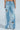 Seen from the back, a person wears the PICKING PETALS FLORAL AND LACE DETAIL DENIM PANTS—light blue, mid-rise jeans featuring wide legs with distressed rips, floral embroidery, and white lace patches—standing barefoot against a light background.