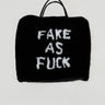 Introducing the IM FAKE ULTRA OVERSIZED FUR TOTE: A black oversized fur tote boldly emblazoned with the phrase "FAKE AS FUCK" in white letters. The bag showcases two sleek faux leather handles and presents a roomy satin-lined interior, set against a plain light gray backdrop to hold all your essentials.