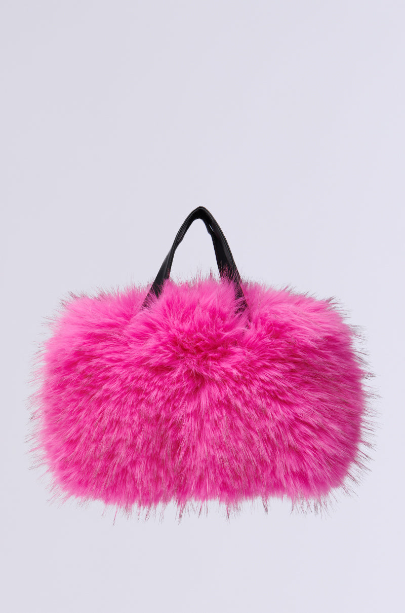 The SABRINA FAUX FUR BAG is a vibrant fuchsia accessory, crafted from faux fur with a shaggy texture. It features two short black handles and a sleek metallic zip closure, creating a bold and trendy look against a plain white background.