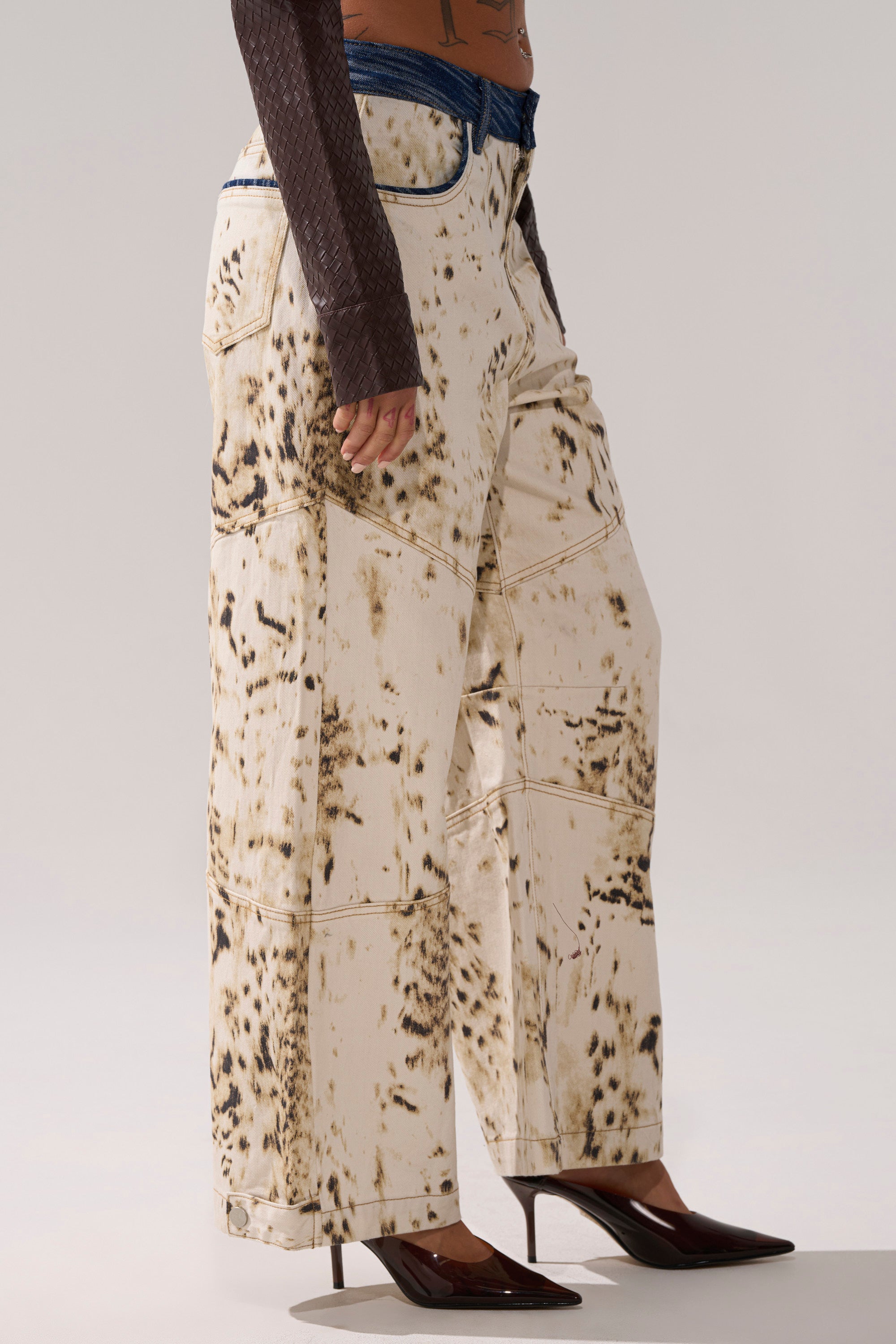 Someone wears BAMBI GIRLY WIDE LEG DENIM—cream-colored, wide-leg pants with a spotted print—paired with brown pointed-toe heels and a textured long-sleeve top, photographed from the side against a plain background. 2