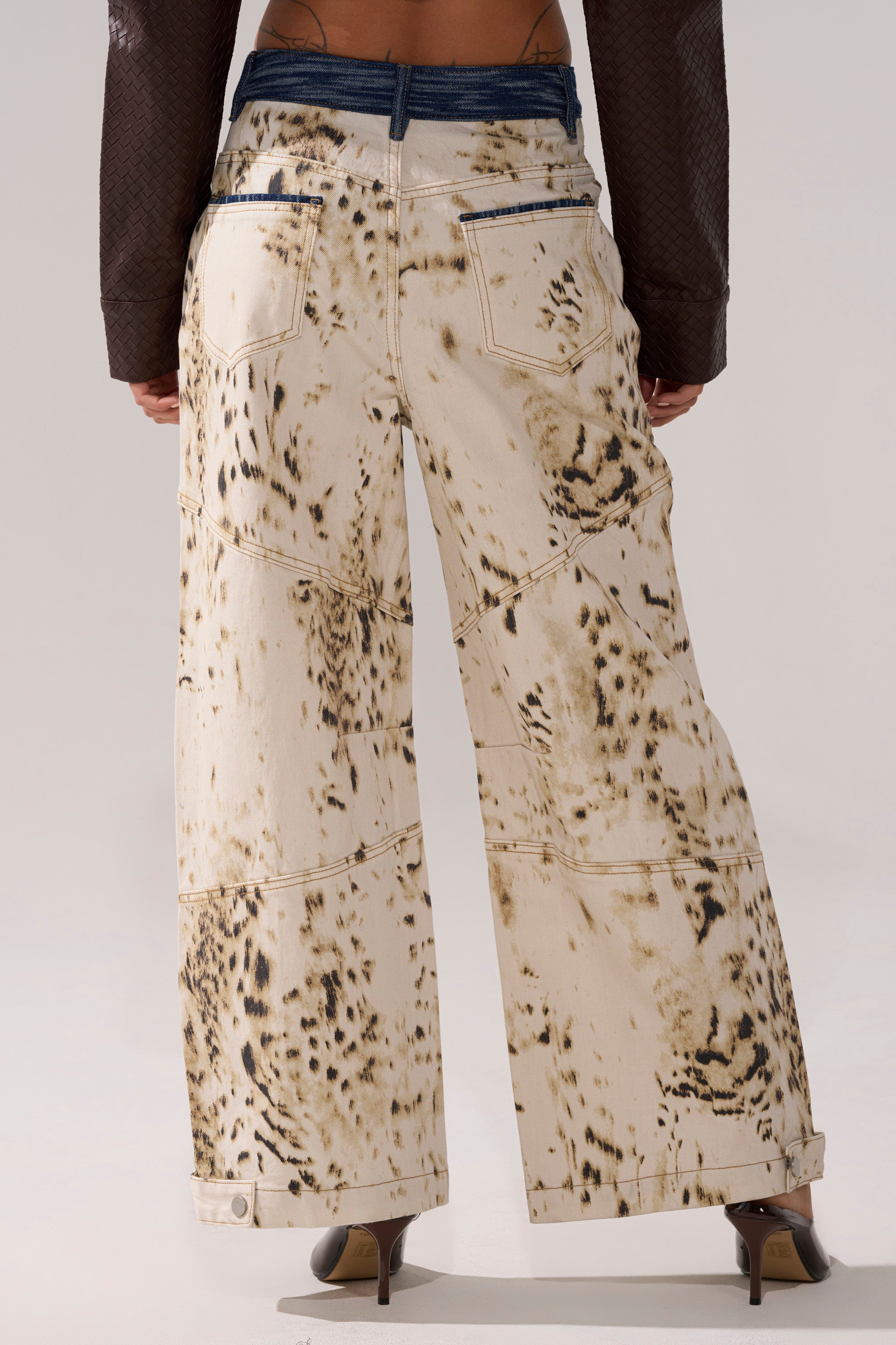 Someone wearing the BAMBI GIRLY WIDE LEG DENIM, high-waisted cream jeans with a brown spotted print, navy waistband and back pockets, paired with brown heels and a dark textured top. 3