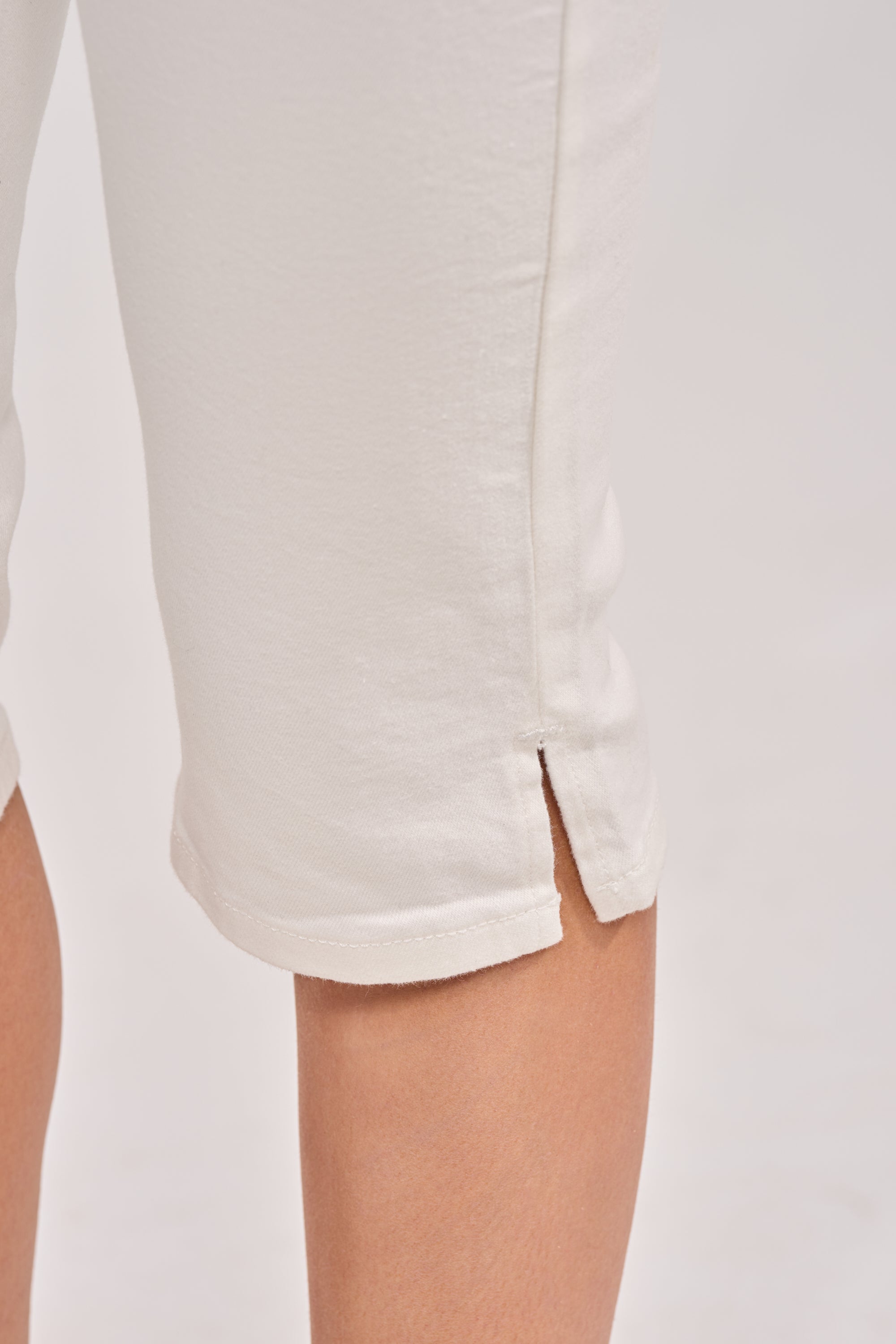 Close-up of a person wearing the CICI DENIM CAPRI in off-white, highlighting the high-rise fit and small side slit at the hem that reveals part of the calf. The plain, light background keeps focus on the capris. 5