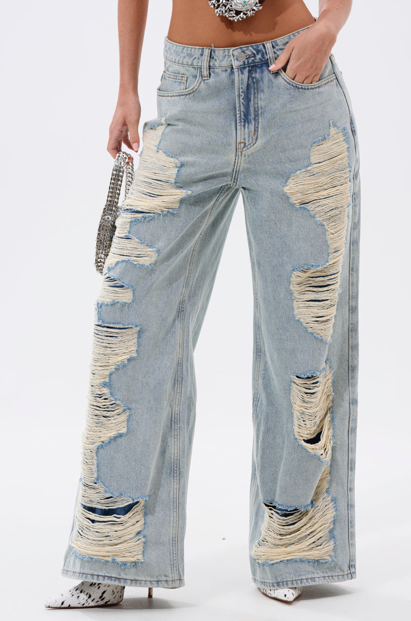 Wearing the CHILL WITH ME DISTRESSED DENIM—high-waisted, light-wash baggy jeans with large distressed rips and frayed edges—they pair it with a small shiny purse and pointed white shoes. 1
