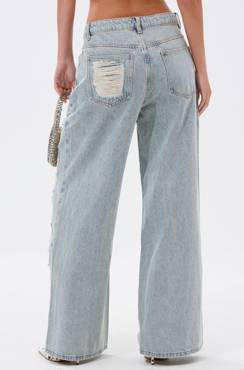 Seen from behind, someone wears CHILL WITH ME DISTRESSED DENIM—light-wash, high-waisted, baggy jeans with a distressed back pocket patch—and carries a small beaded handbag. 4