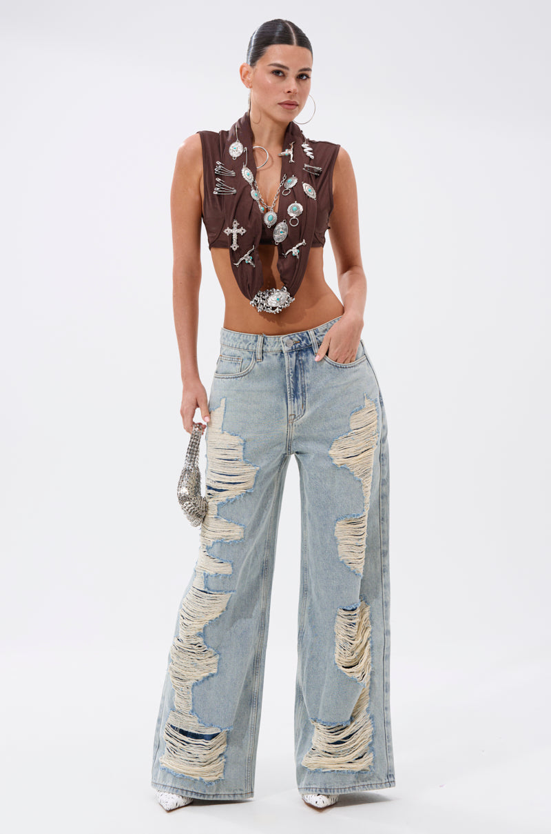 A woman stands confidently in the CHILL WITH ME DISTRESSED DENIM, paired with a brown sleeveless cropped top, silver jewelry, white heels, and a small silver handbag. 5