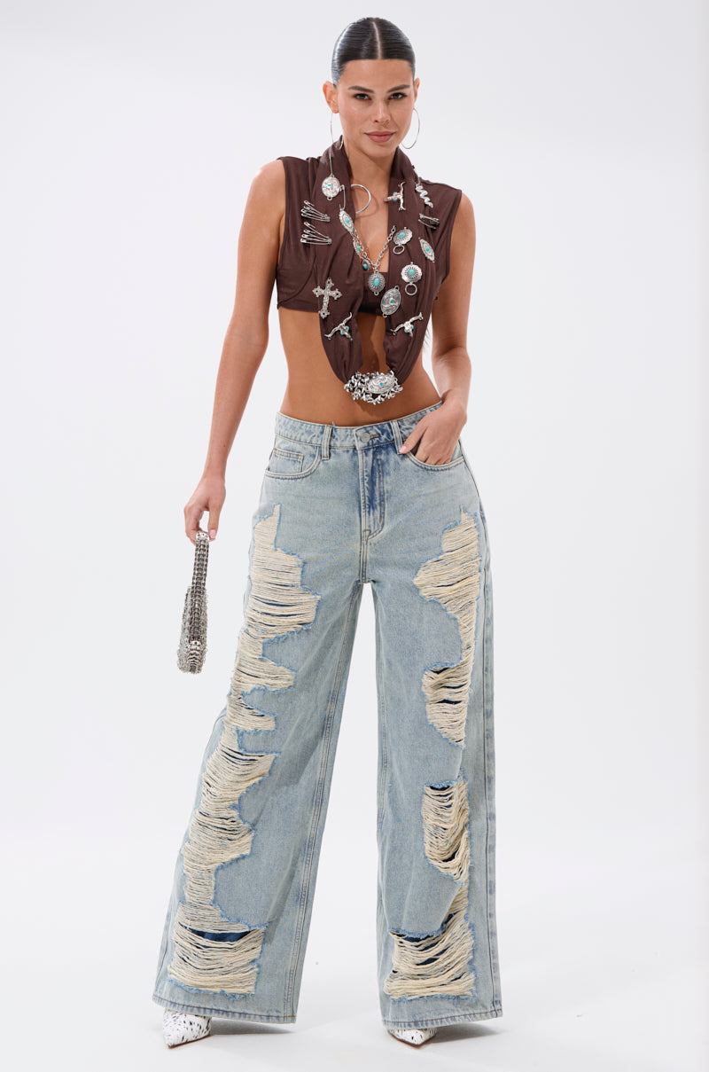 A woman poses in a sleeveless brown metallic-embellished crop top paired with CHILL WITH ME DISTRESSED DENIM, white pointed shoes, and carries a small silver beaded purse. 6