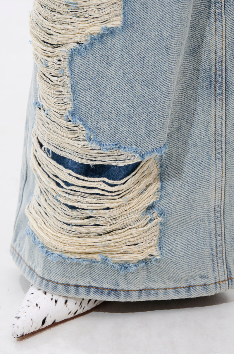 A close-up of the CHILL WITH ME DISTRESSED DENIM jeans in light blue, featuring large frayed holes and a white pointed-toe shoe with black speckles peeking out from under the hem. 8