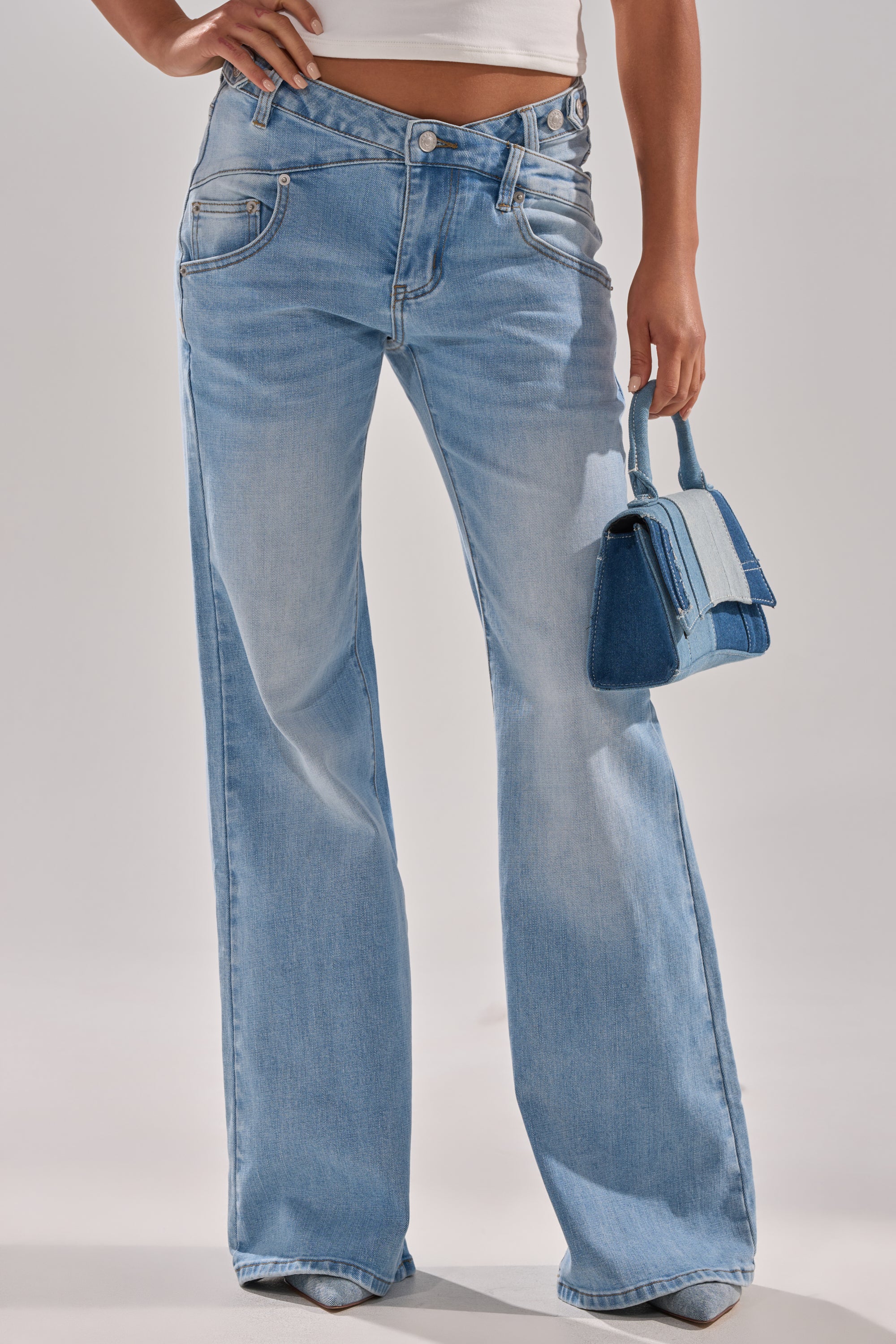 Model wears WON'T LOSE MYSELF WIDE-LEG BLUE DENIM jeans in a light wash with a white crop top, holding a small blue handbag. Only her legs and torso are shown against a plain, light background. 2