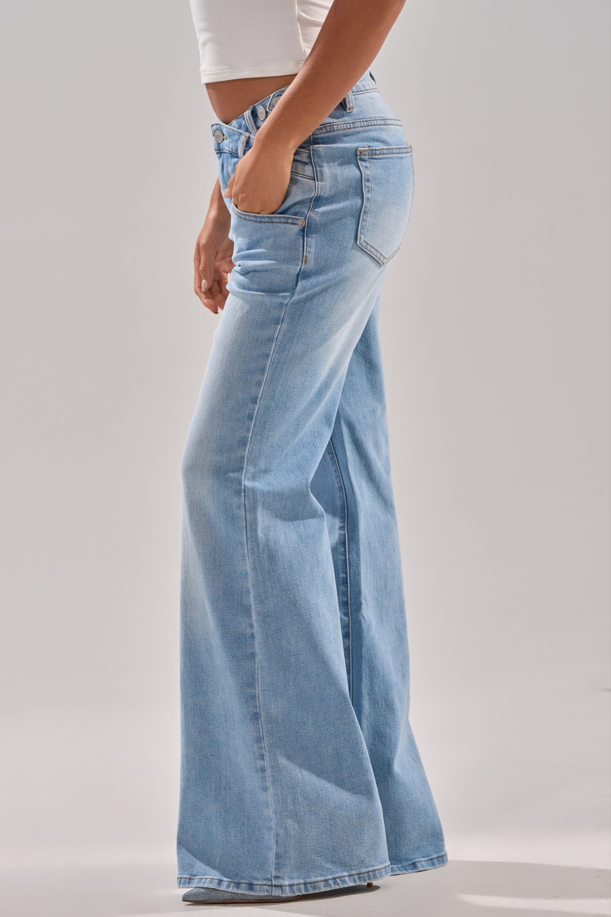 A person in the WON'T LOSE MYSELF WIDE-LEG BLUE DENIM jeans and a white crop top poses with one hand in their pocket against a plain light background. 4