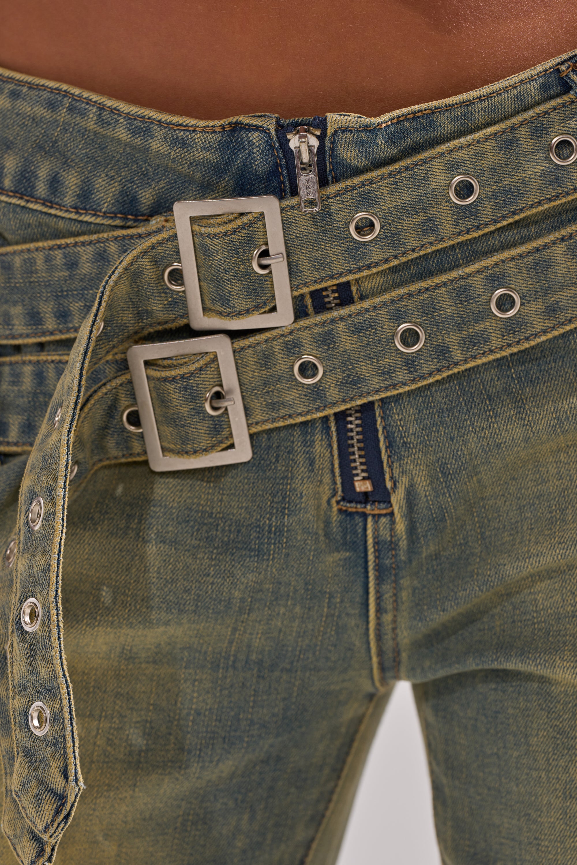 Close-up of a person wearing the JUST LIKE THAT STRAIGHT-LEG DENIM WITH BUCKLE: blue-green straight-leg jeans paired with a double silver buckle belt with two rows of grommets, looped through the mid-rise waistband with visible zipper and stitching.