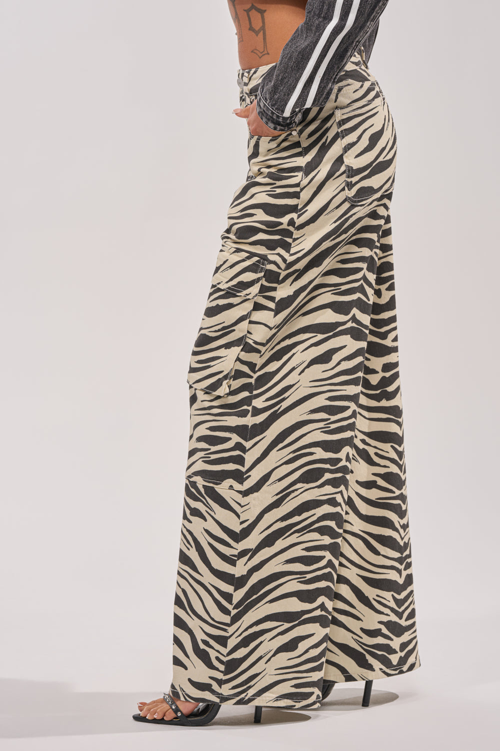 A person wearing the IN THE WILD ZEBRA DENIM skirt with large side pockets and black high-heeled sandals, shown from the side against a plain background. 2