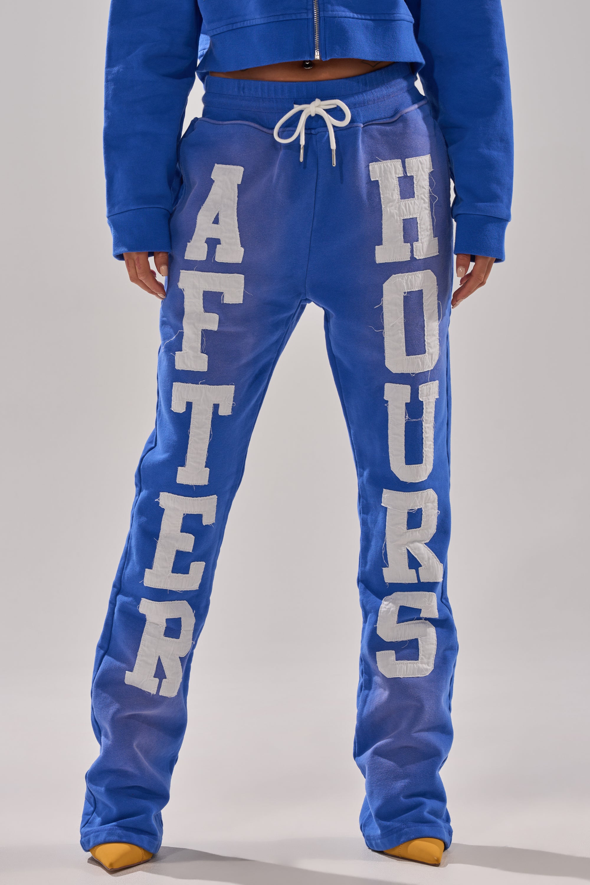 Wearing AFTER HOURS FLARED SWEATPANT with “AFTER” on the left leg and “HOURS” on the right, styled with a matching blue jacket and yellow shoes for a bold, coordinated look. 1