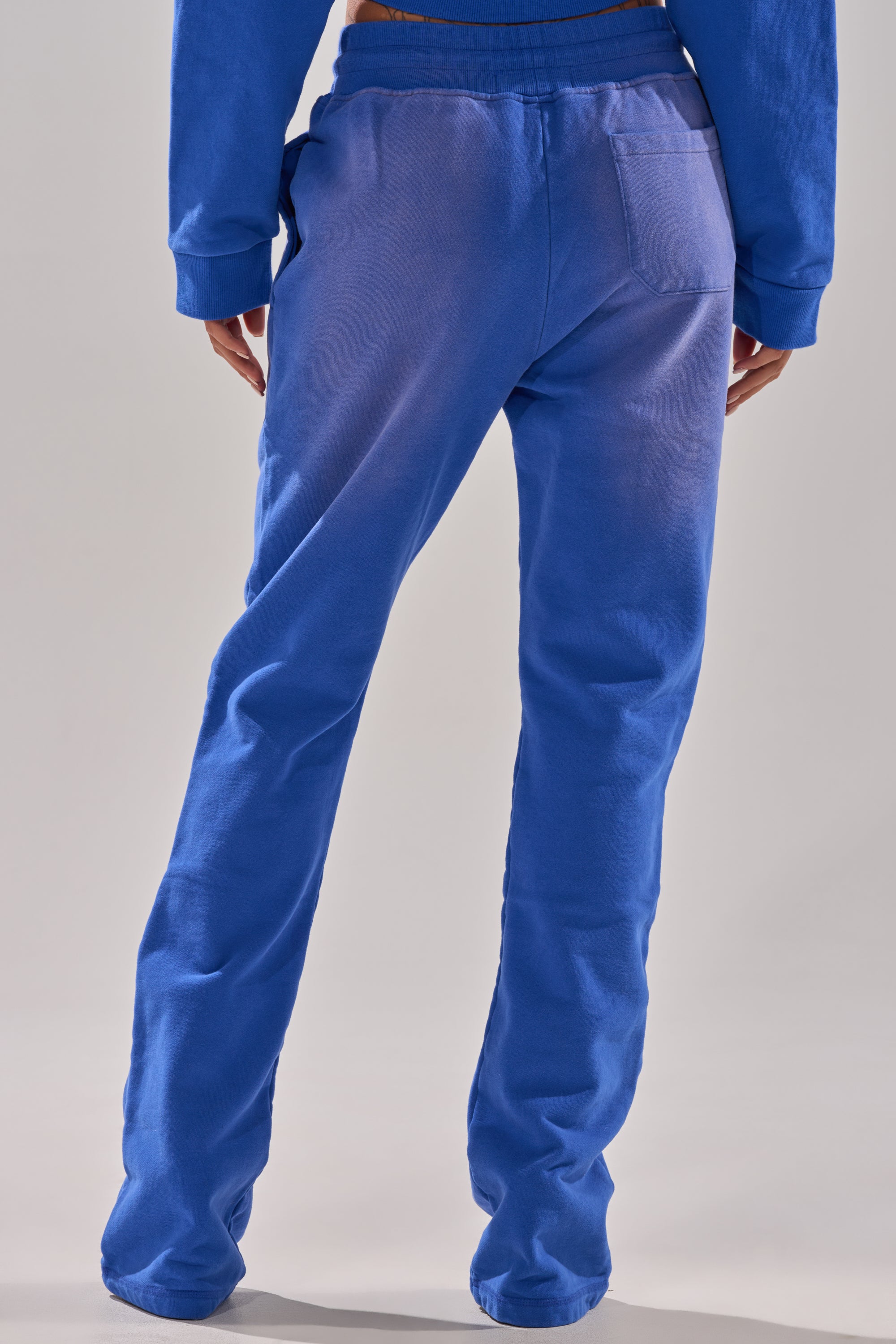 A person is shown from the back wearing the AFTER HOURS FLARED SWEATPANT in bright blue with a matching sweatshirt. The high-rise, relaxed-fit pants feature a single rear pocket, set against a plain neutral background. 3