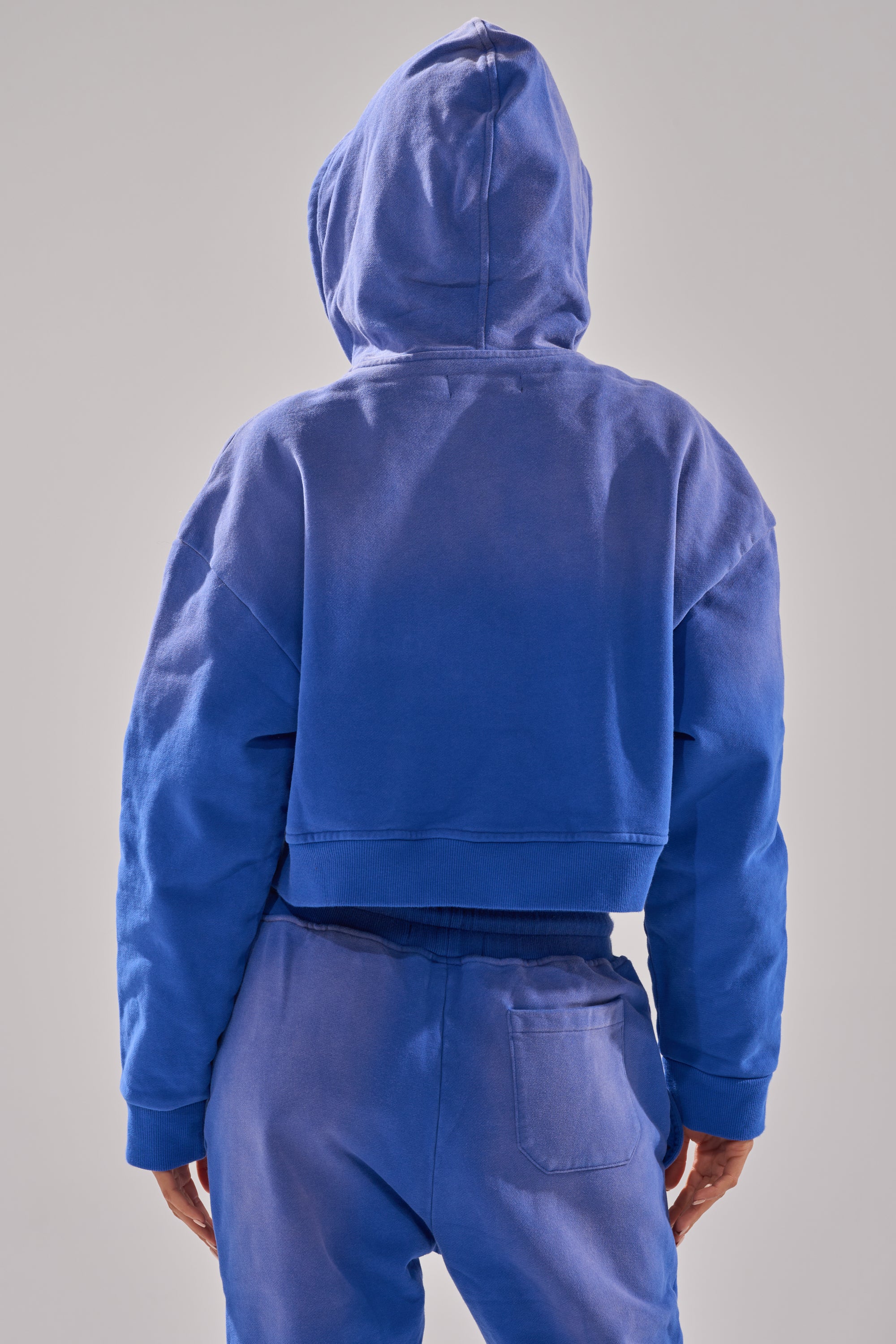 Wearing the oversized AFTER HOURS ZIP UP SWEATSHIRT and matching sweatpants, a person stands with their back to the camera, hood up and hands by their sides, set against a plain grey background.
