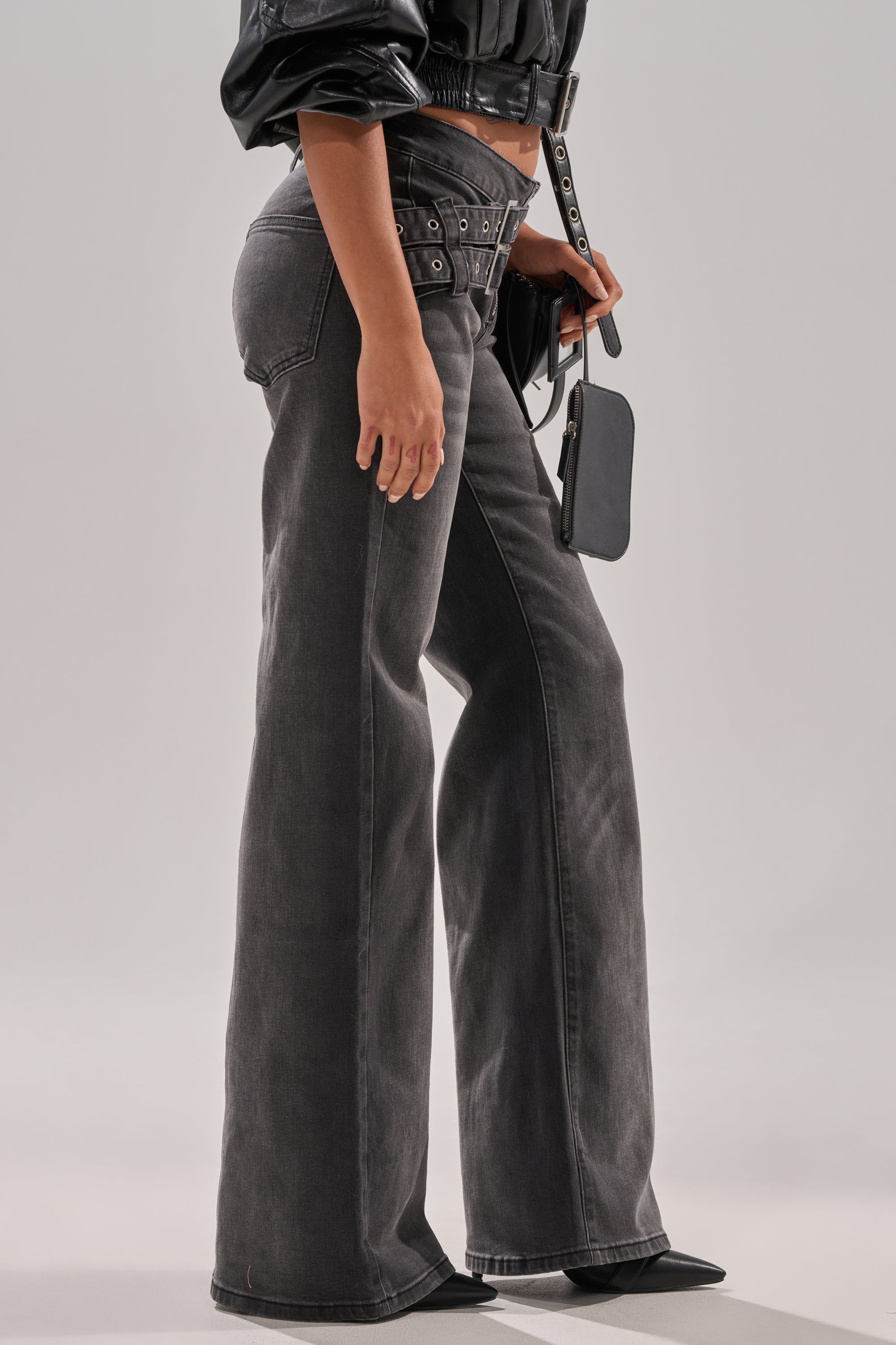 Wearing WONT LOSE MYSELF WIDE LEG DENIM—high-waisted, washed-black wide-leg jeans with an adjustable waistbelt—styled with a cropped black leather jacket, pointed-toe black shoes, and a small black handbag. 3