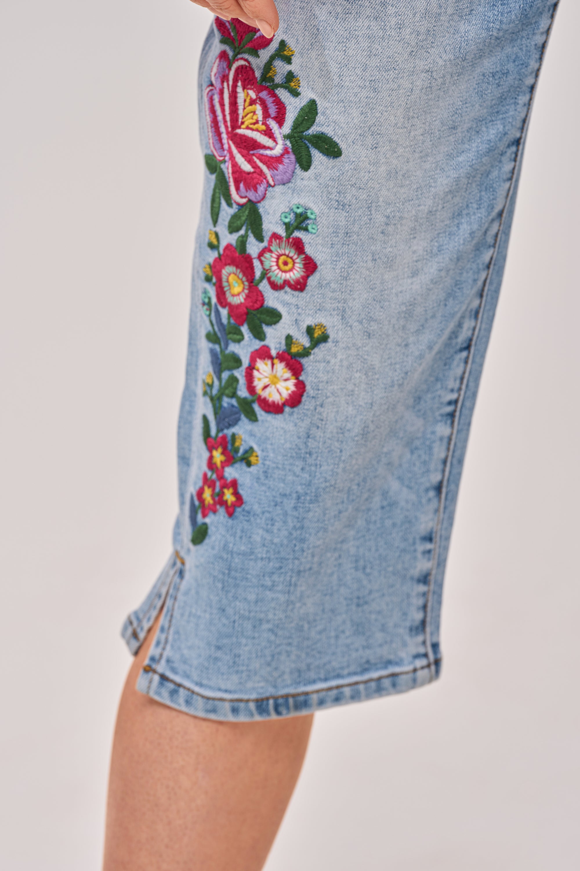 A close-up of a leg in the GIVE ME FLOWERS FLORAL CAPRI, featuring colorful embroidered flowers and a hem slit—perfect for spring style. 5