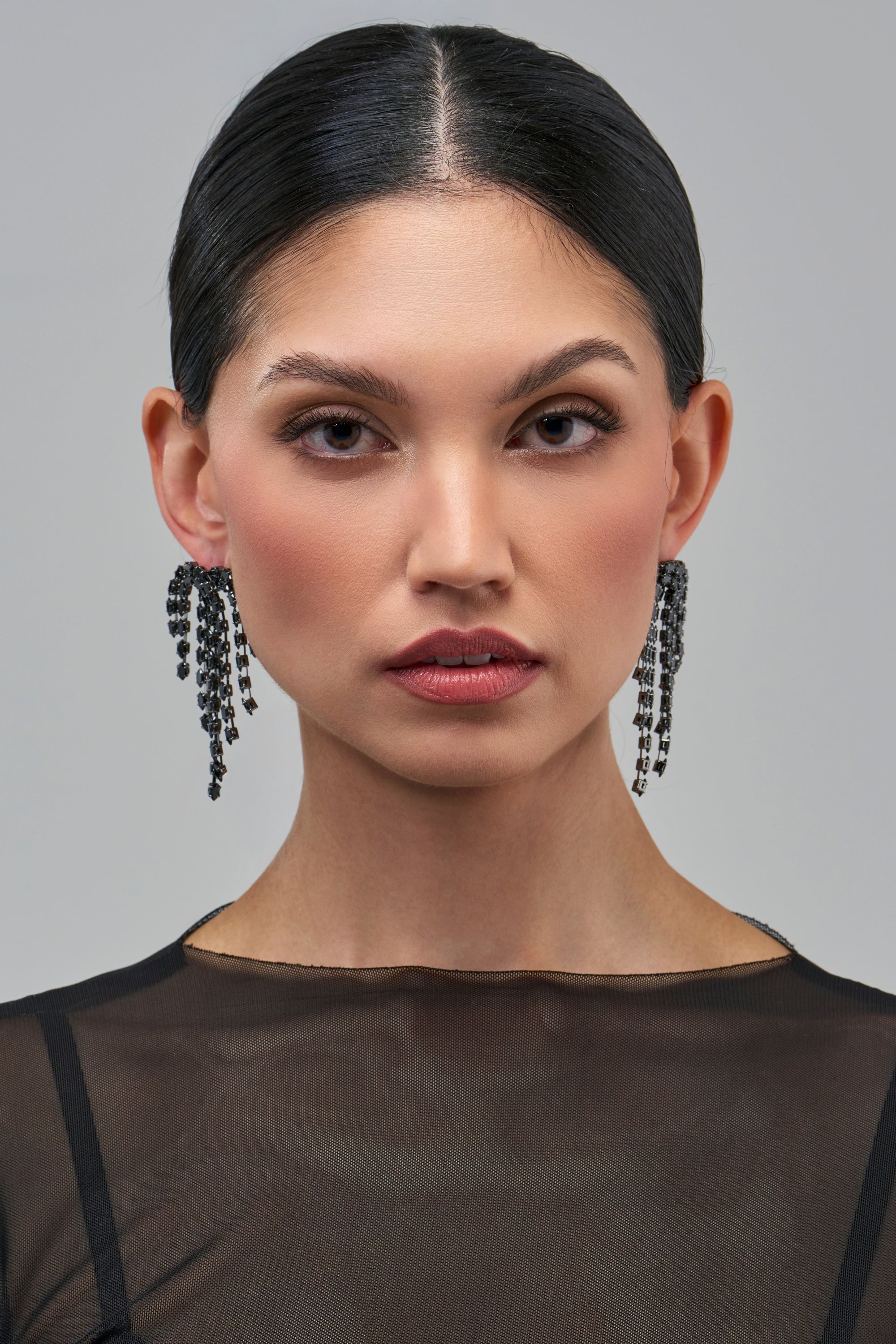 A woman wearing MIDNIGHT FRINGE CRYSTAL EARRINGS, which feature long, black tiered crystal fringe.