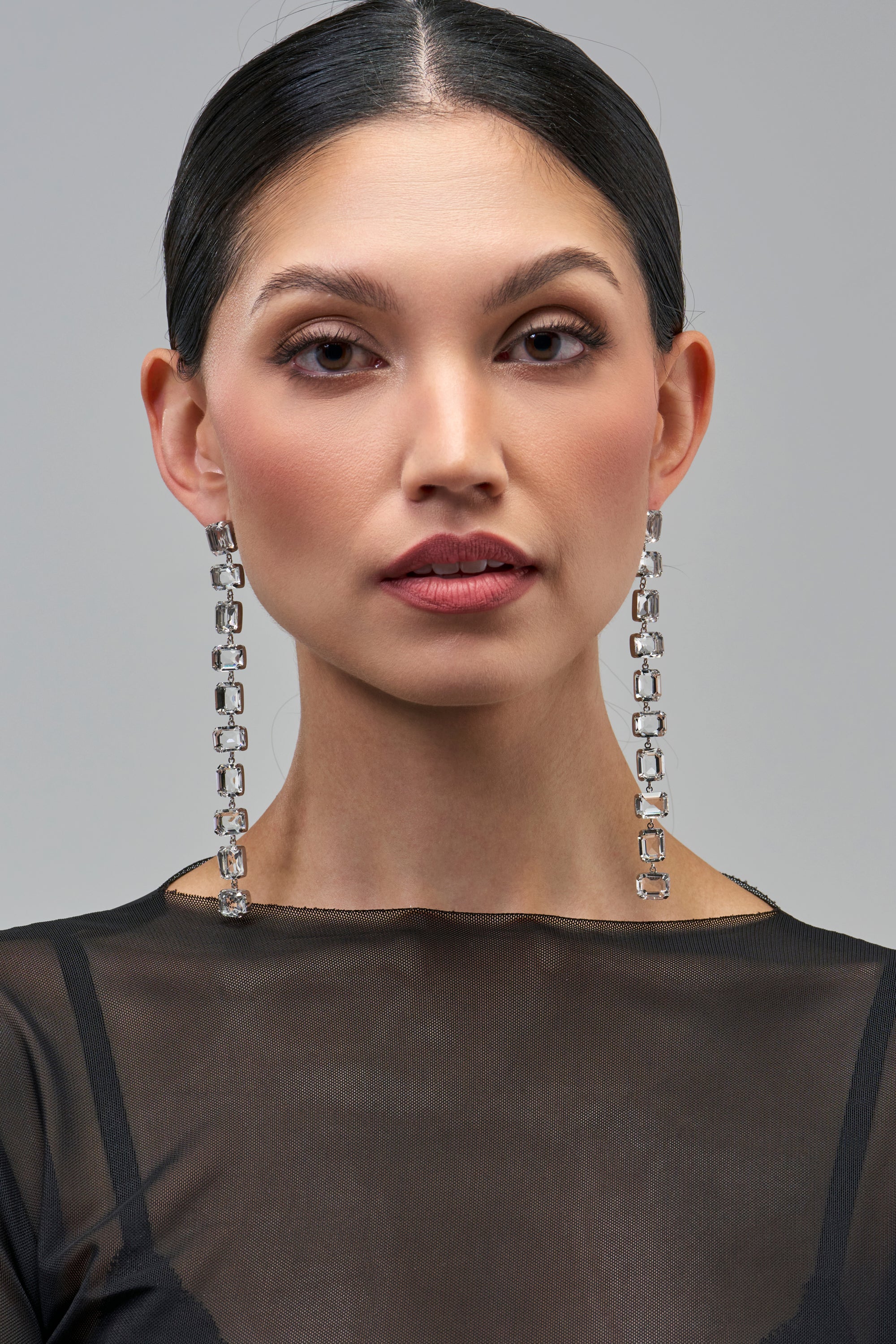 A model wearing ICE QUEEN LINEAR DROP EARRINGS, which are long, silver-tone rhinestone drop earrings composed of rectangular, clear stones.