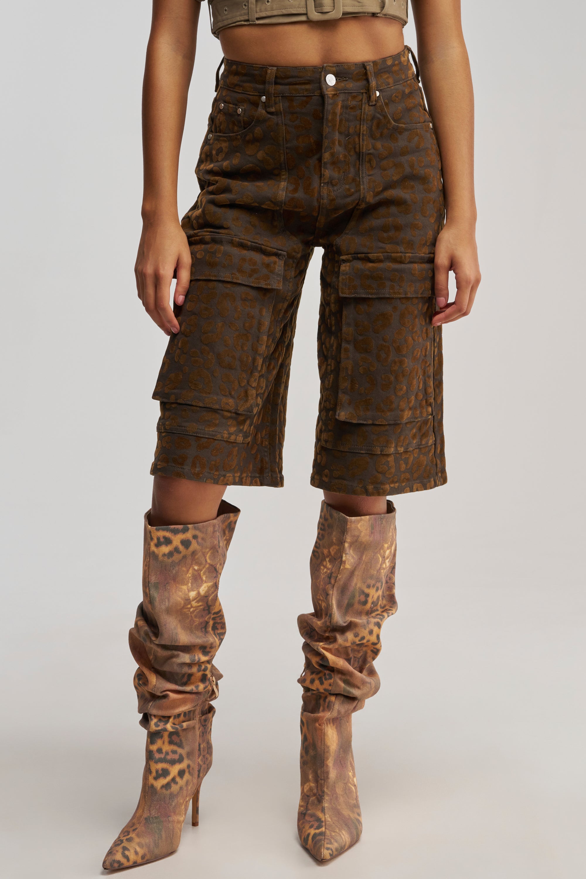 A person wearing tan and cheetah print apparel—including the CHEETAH GIRL BERMUDA SHORT and matching patterned slouchy high-heeled boots—stands against a plain background.