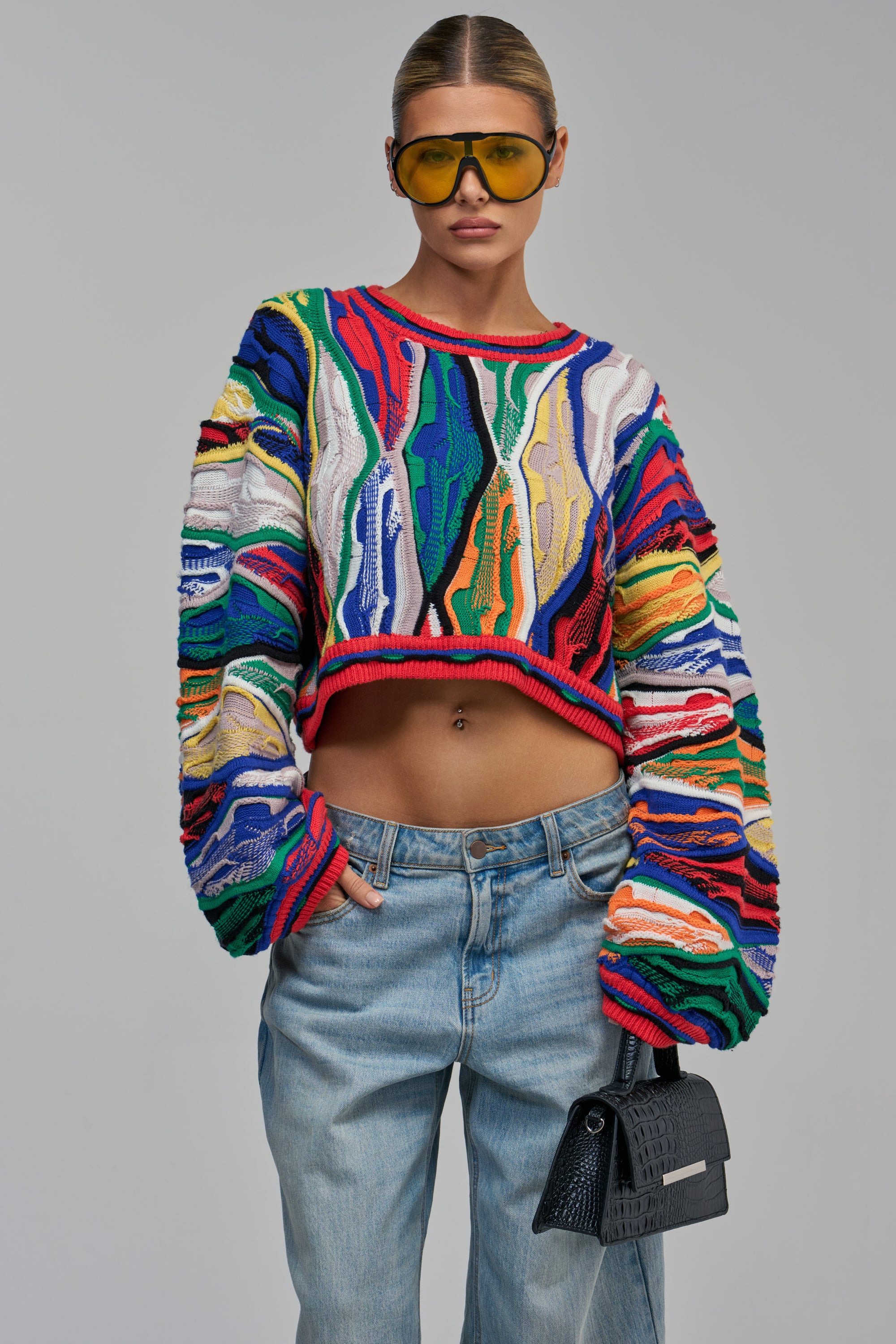 A person wearing a multicolored, distressed GOOD DAYS VINTAGE CROPPED SWEATER with long sleeves and light-wash blue jeans.