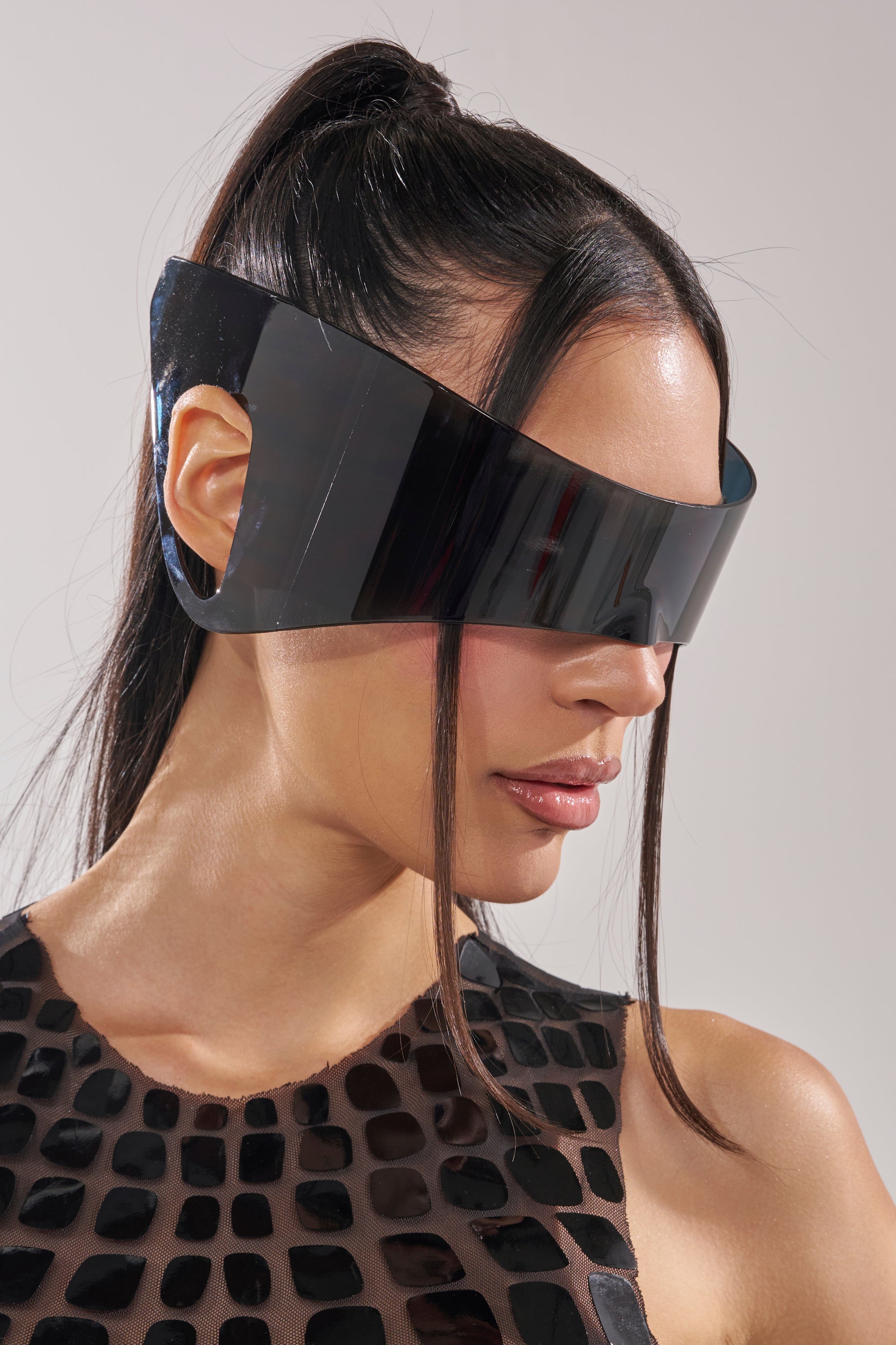 A woman with long dark hair in a high ponytail wears IRVY SUNGLASSES and a sleeveless black textured dress, looking to the side against a plain background. 0