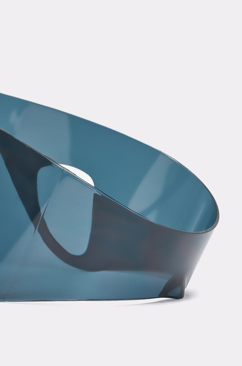 A close-up of a twisted, translucent blue plastic strip against a plain light background, echoing the sweeping curves and sleek reflections inspired by IRVY SUNGLASSES. 4