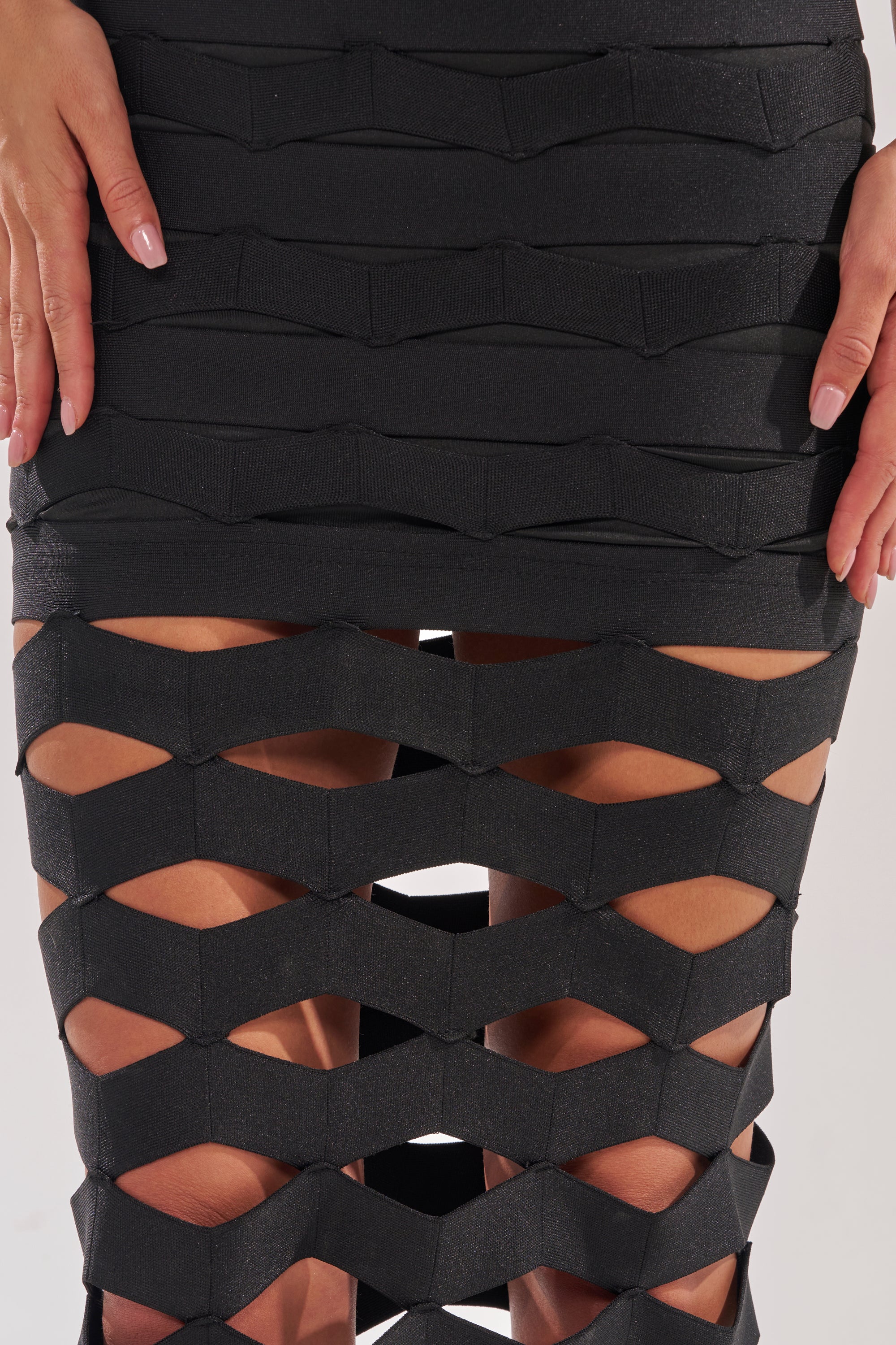 Wearing the STREET CHIC MAXI DRESS with bold geometric cutouts and a black skirt that reveals skin at the thighs, the person poses with hands on hips, highlighting their light pink nail polish. 6