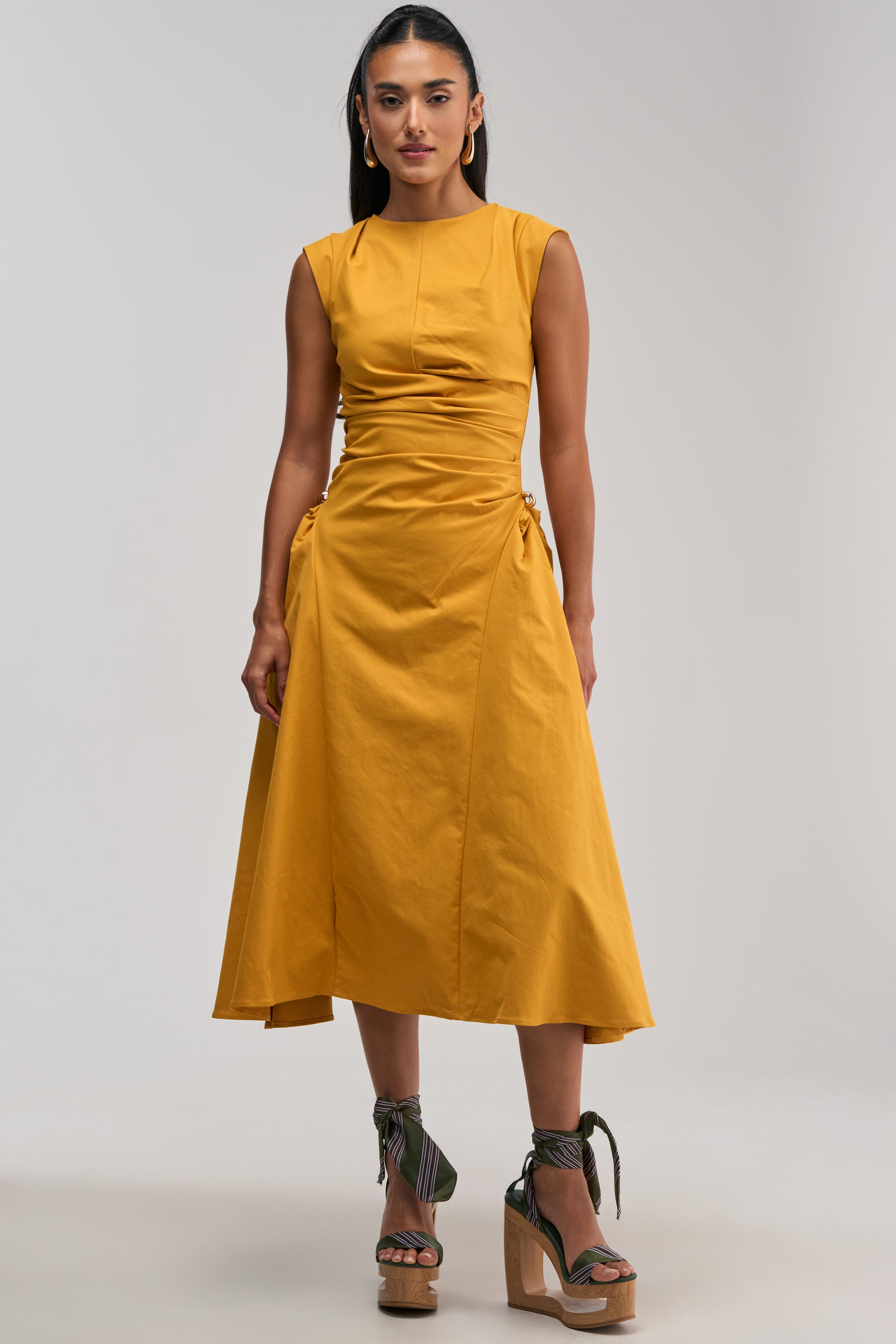 Wearing the IT’S MY TIME MIDI DRESS IN MUSTARD—a sleeveless, ruched midi dress with a cinched waist—paired with olive green strappy cork wedge sandals and gold hoop earrings makes for the perfect business casual look for your next work event.