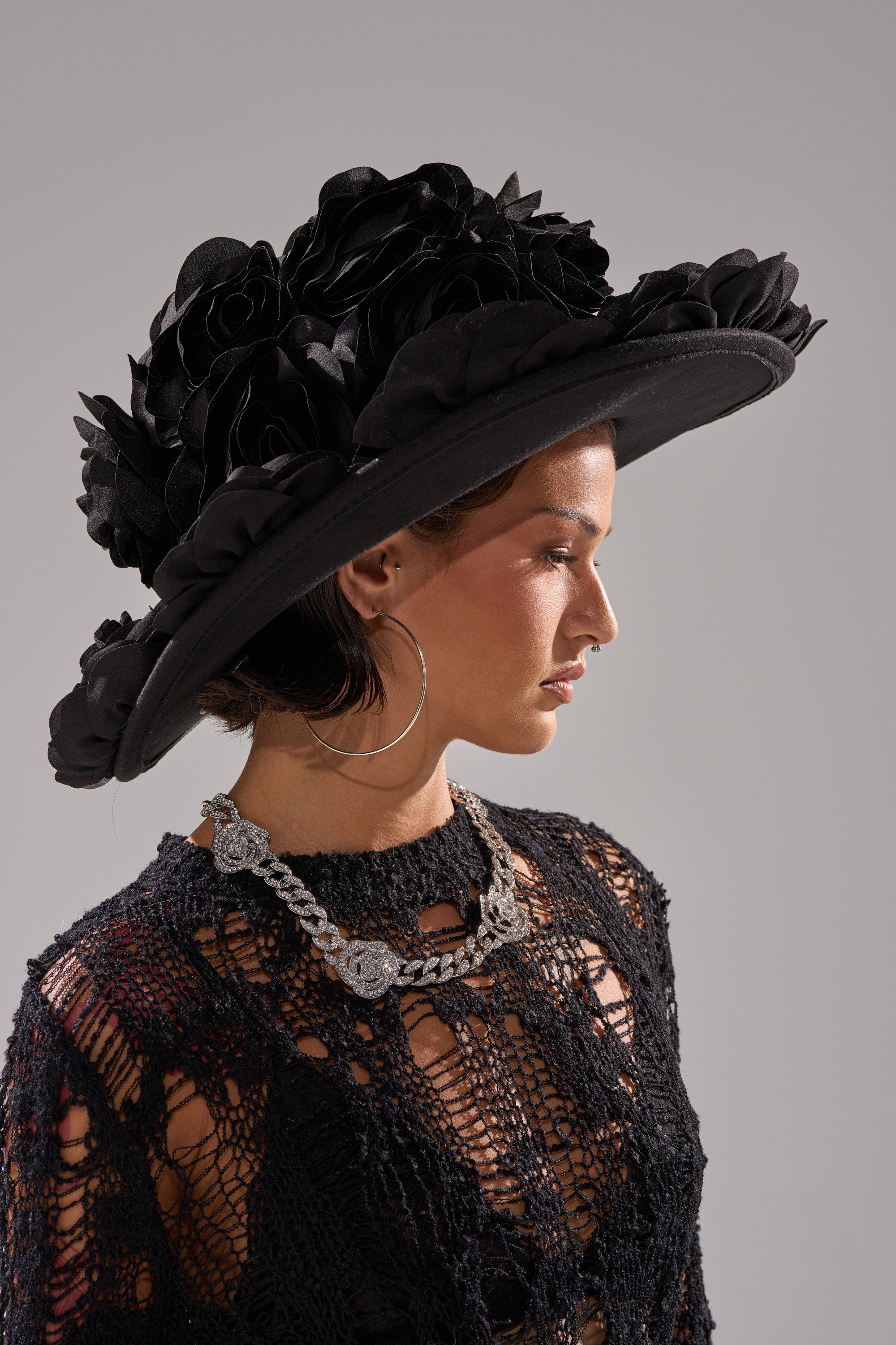 A woman in profile models the DARK ROSE FLORAL COWBOY HAT, featuring striking 3D floral details, paired with hoop earrings, a silver necklace, and a black lace top against a plain gray background.
