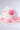 The TO THE RACES FLOWER HAT by AKIRA Label is a white cowboy hat adorned with soft, translucent petals and bright pink fabric flowers, showcased against a plain, softly lit background.