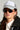 A person wearing the AND THATS THAT TRUCKER HAT, which is white and adorned with the phrase "Never Too Much," along with sunglasses, large hoop earrings, and a black jacket. The hat boasts rhinestone accents on the brim and has an adjustable snapback closure for a perfect fit.