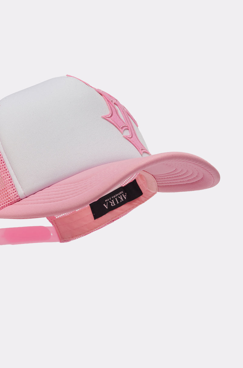 The CROSS ME PATCH HAT is a white and pink trucker cap with a pink embroidered logo, street-style design, and an adjustable pink snapback strap labeled “ATRA.”. 6