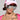 A person sporting the MOTHER TRUCKER HAT IN PINK, complemented by large reflective sunglasses, and accessorized with silver jewelry like a chain necklace and hoop earrings. They display an arm tattoo and wear a pink outfit with an adjustable snapback closure.